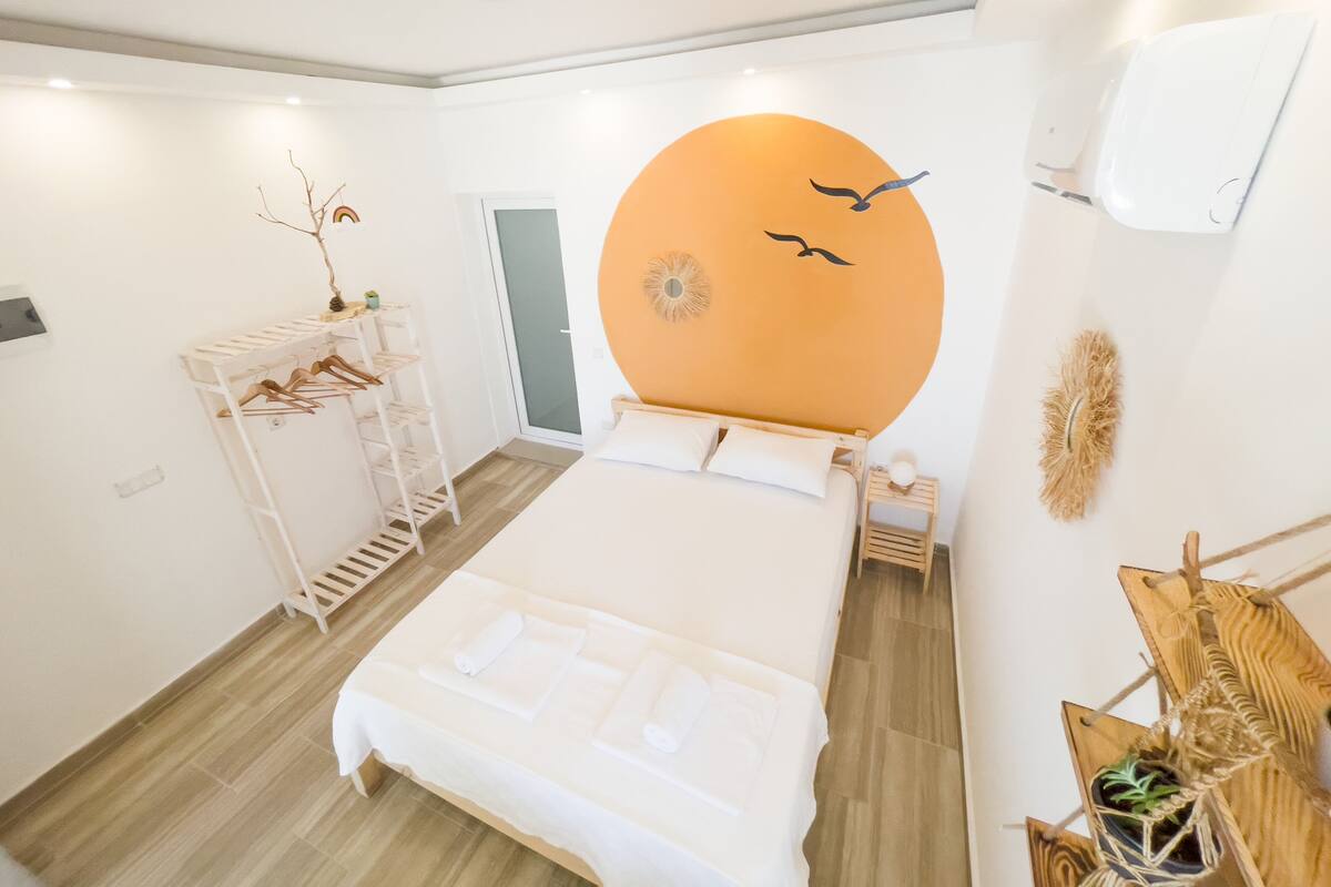 A modern bedroom with a large bed, a wooden shelf with clothes, a small plant, and a wall decoration.