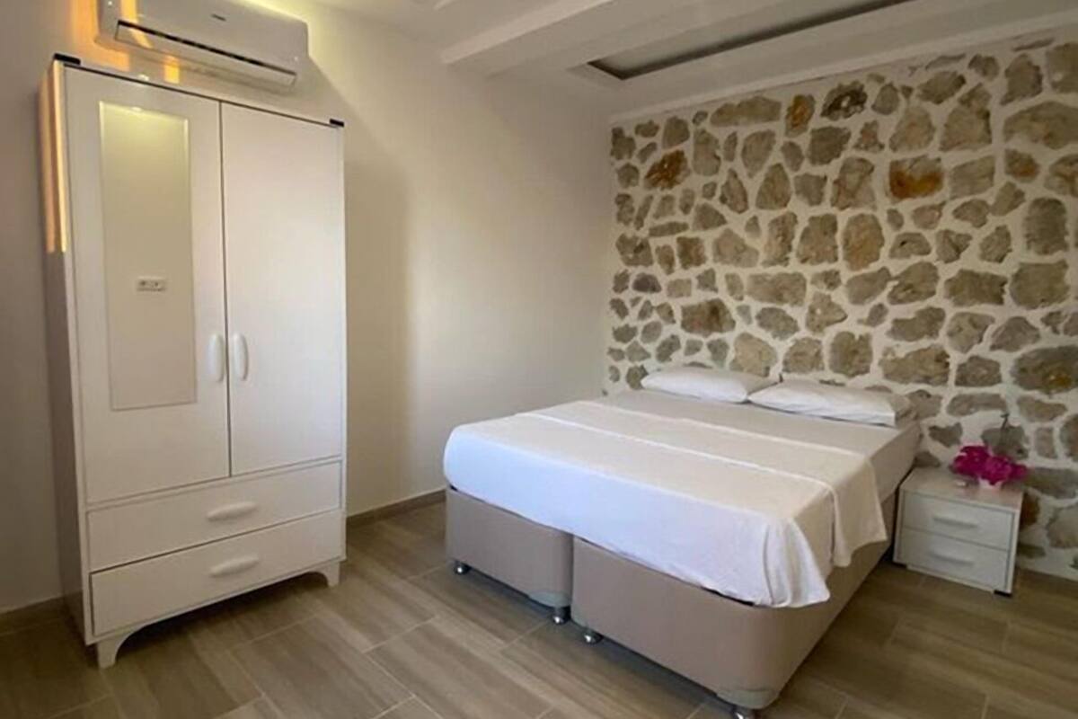 A bedroom with a stone wall, a bed, a wardrobe, and a nightstand.