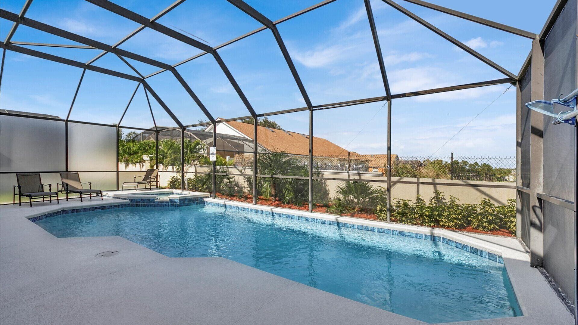 An indoor swimming pool with a clear view of the surrounding area, including a building with a red roof and greenery.