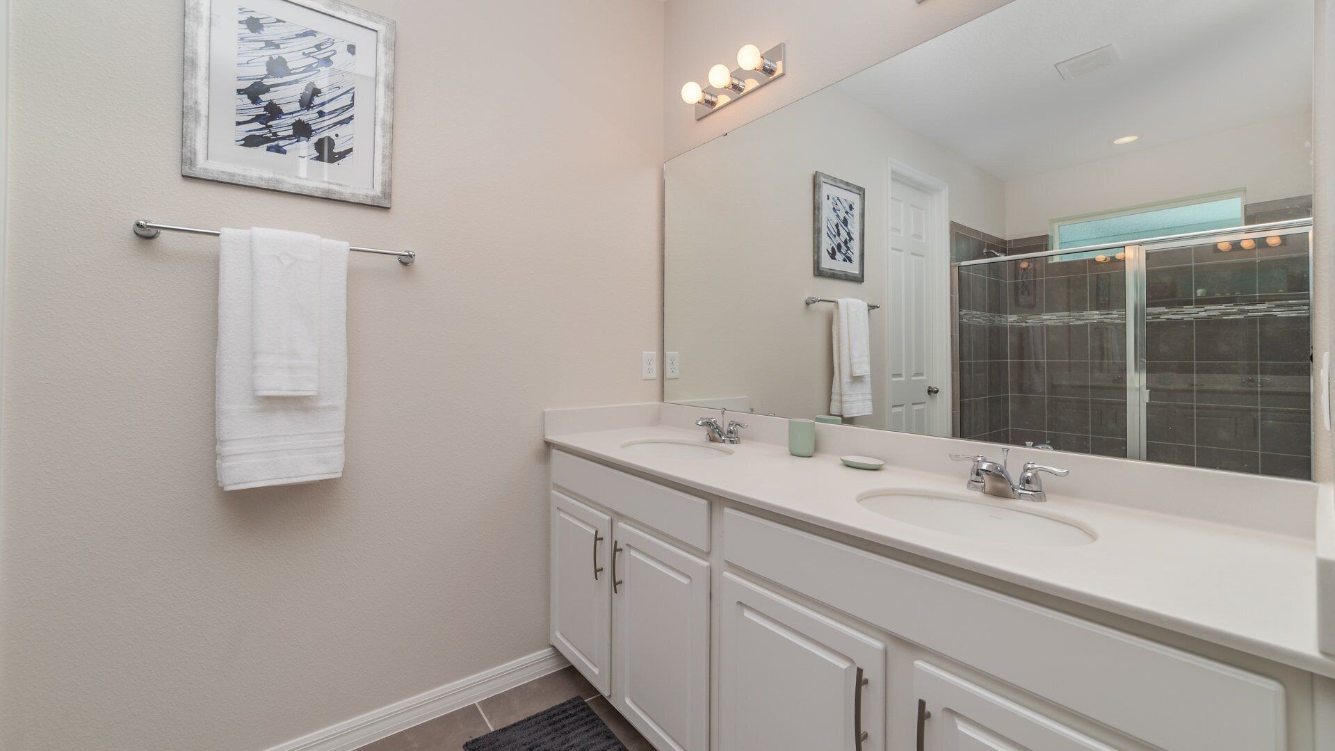 A modern bathroom with two sinks, a large mirror, and a towel rack.