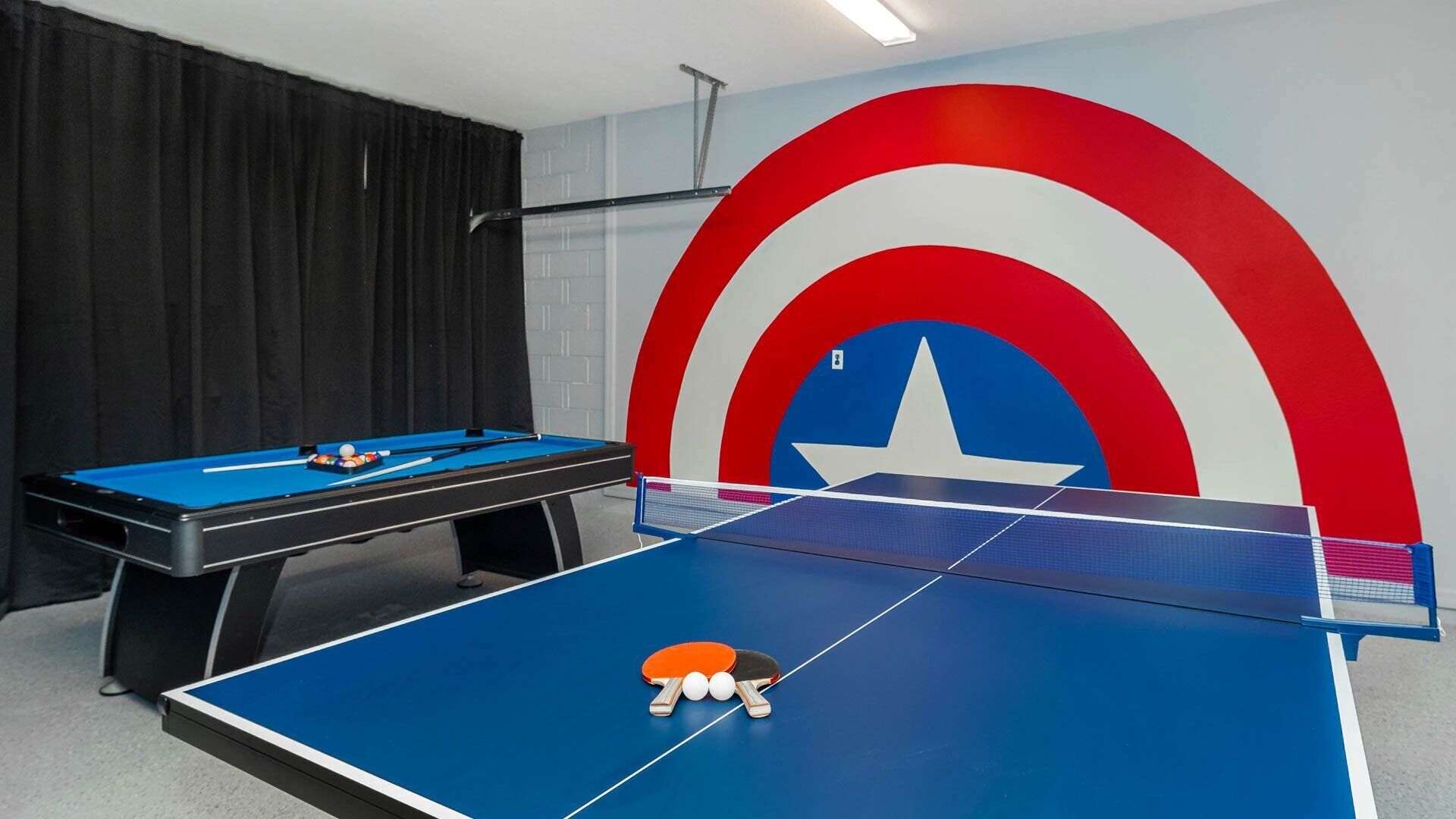 Una habitación con mesa de billar y mesa de ping pong, ambas con diseño del escudo del Capitán América.