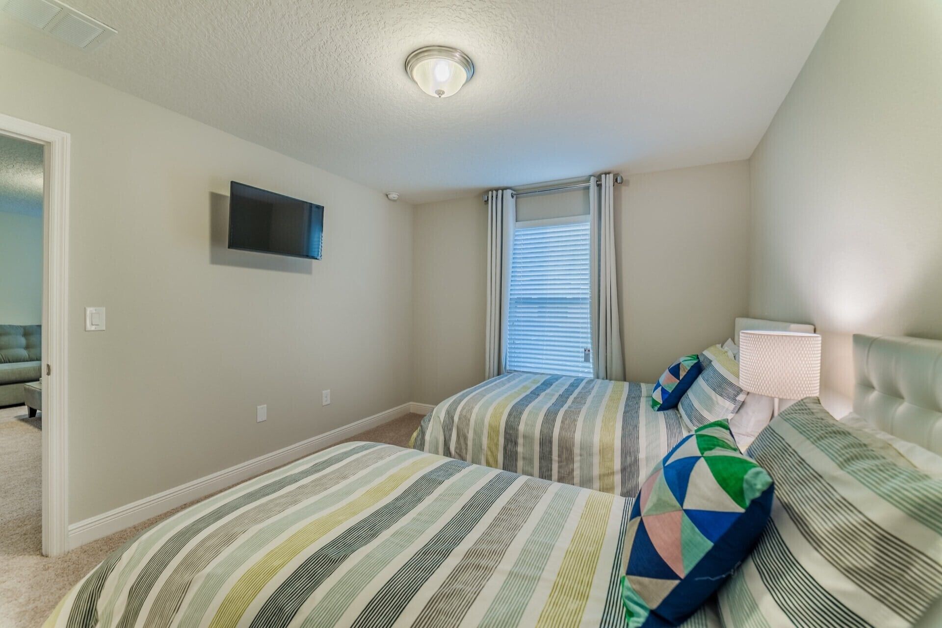 A bedroom with two beds, a TV, a window with blinds, and a lamp.