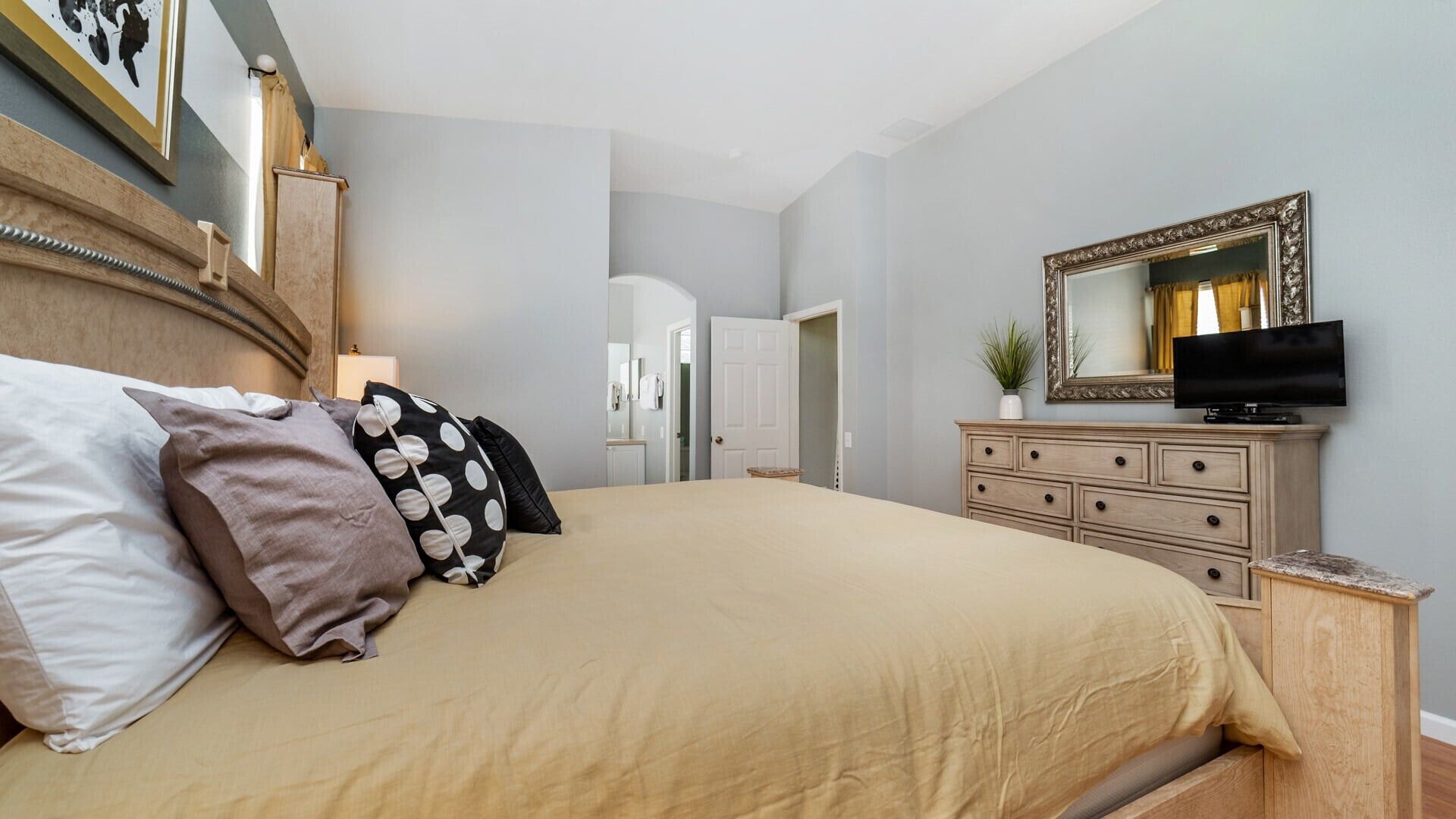 A bedroom with a bed, dresser, television, and a mirror.