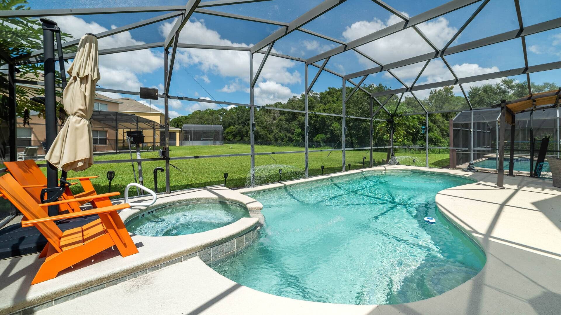 Una piscina con área techada, una silla de descanso y vistas a un área verde y edificios al fondo.