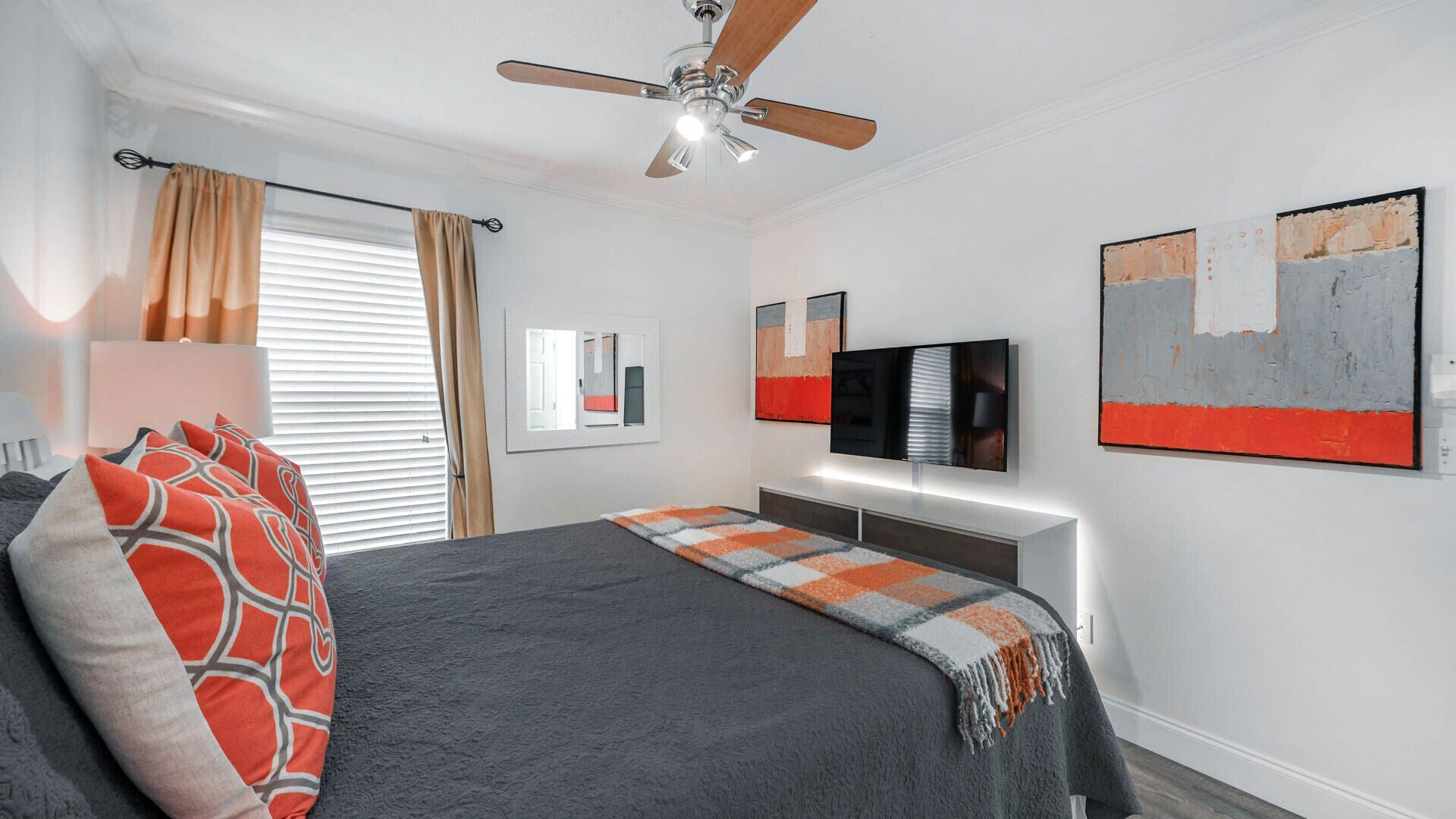Camera da letto moderna con letto, ventilatore a soffitto, televisore, opere d'arte e una finestra con tende.
