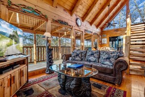 A cozy cabin interior with a wooden ceiling, a sofa with animal prints, a glass coffee table, and a television on a wooden stand. - Romantic, secluded, relaxing retreat, arcade game,hot tub, wooden cabin, private (Sevierville)