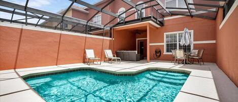 A swimming pool with lounge chairs, a covered patio, and a building with a red exterior.