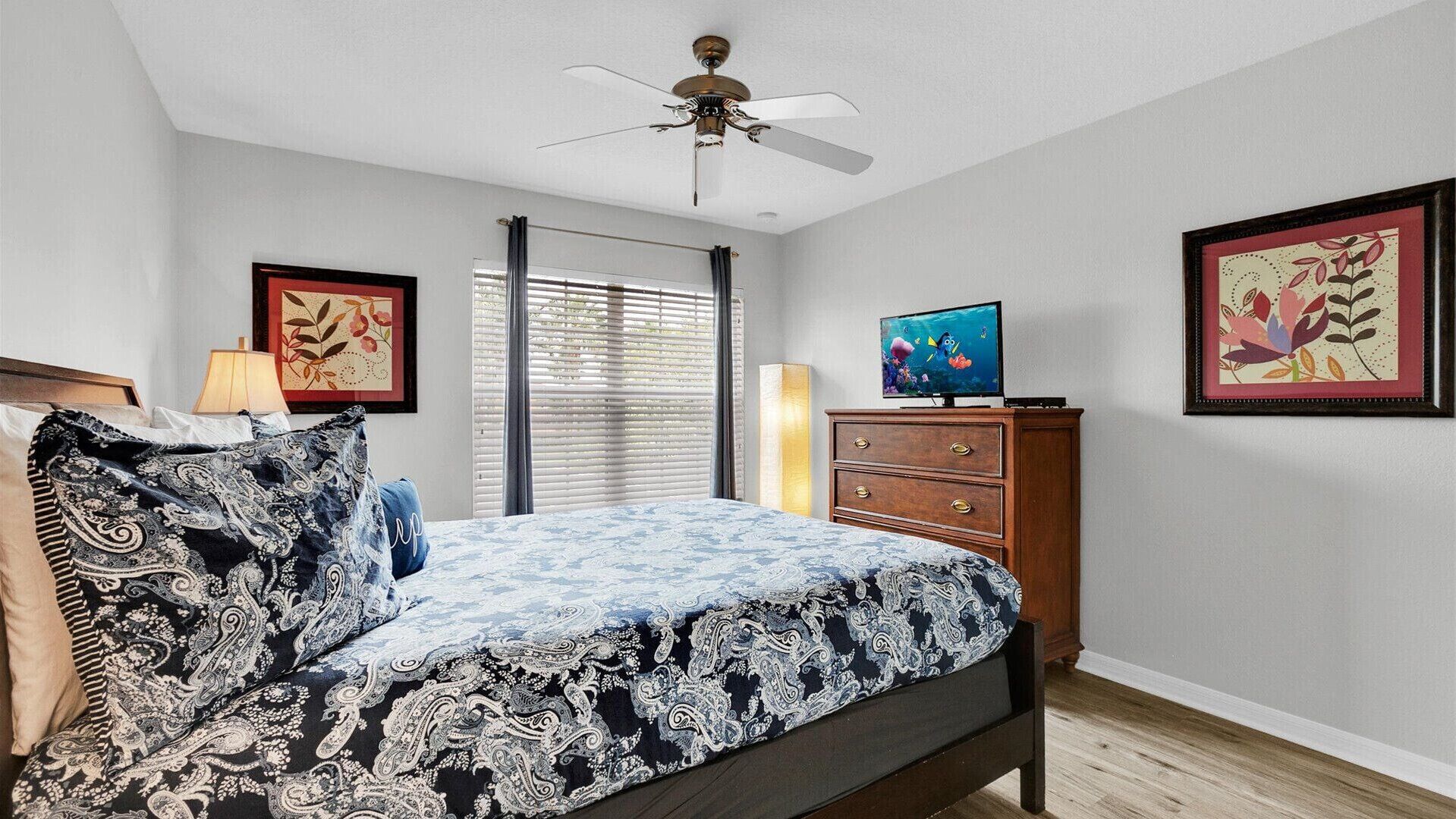 A bedroom with a bed, a dresser, a ceiling fan, and two framed pictures on the wall.