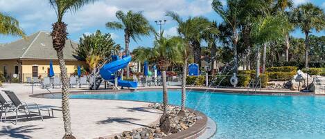 A pool area with a water slide, lounge chairs, and palm trees.
