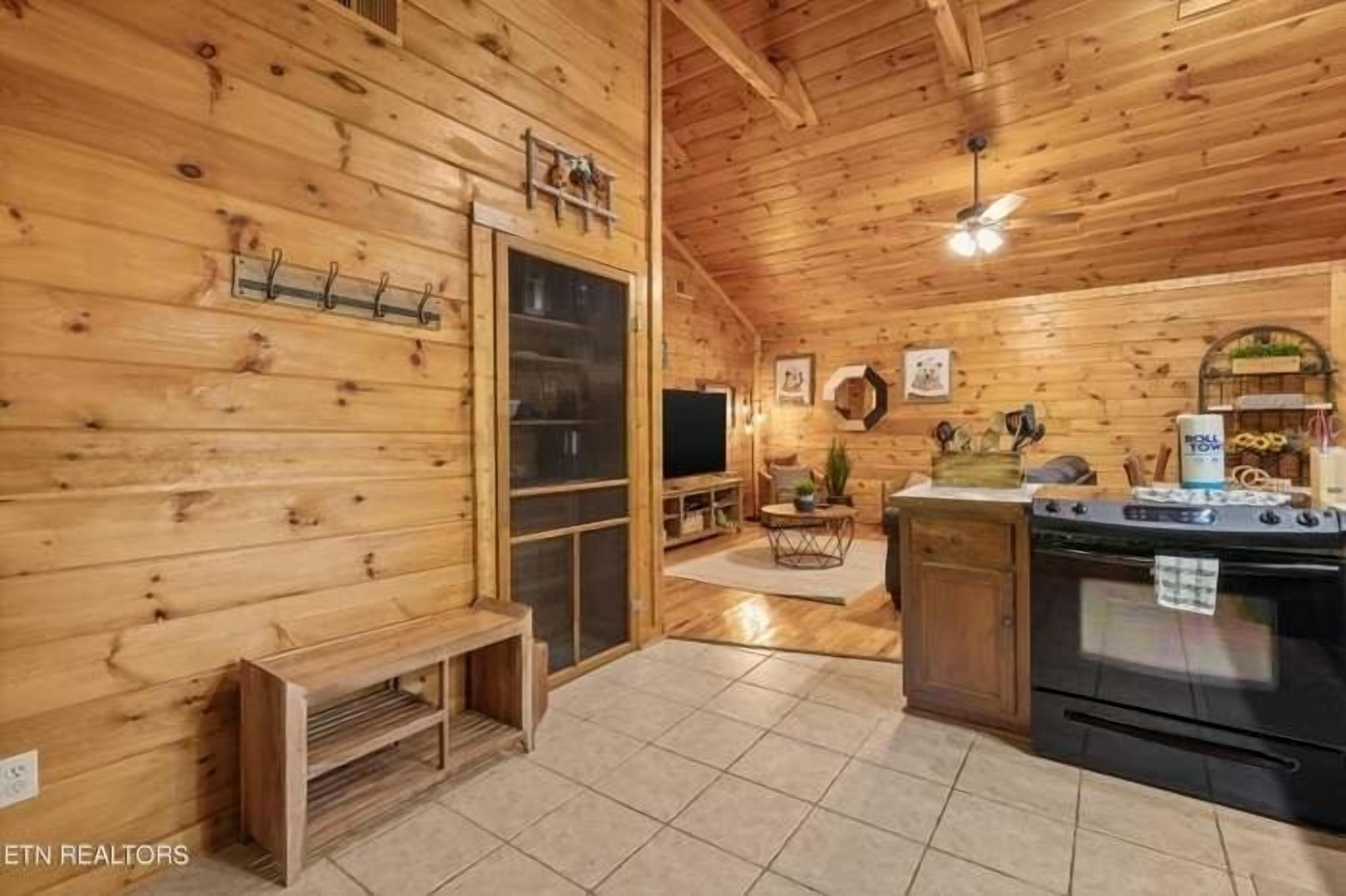 A wooden cabin interior with a kitchen area, a bench, and a television.