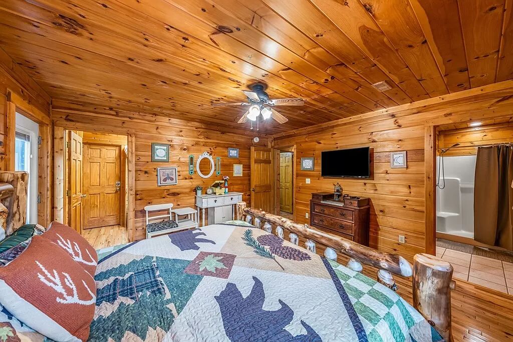 Interior de una cabaña de troncos con una cama, un televisor, techo de madera y chimenea.