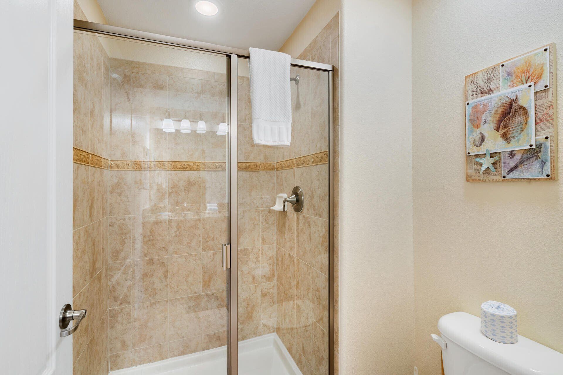 A bathroom with a glass shower enclosure, a toilet, and a wall-mounted toilet paper holder.