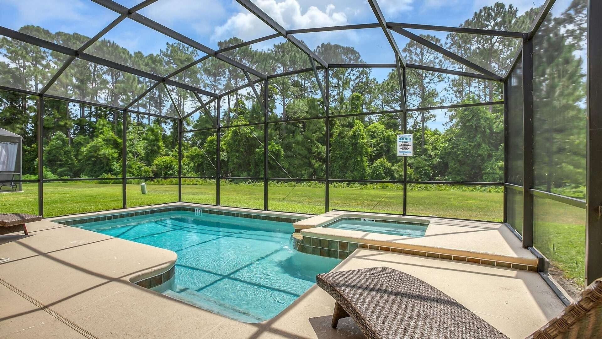 A covered outdoor swimming pool with lounge chairs and a sign indicating pool rules.