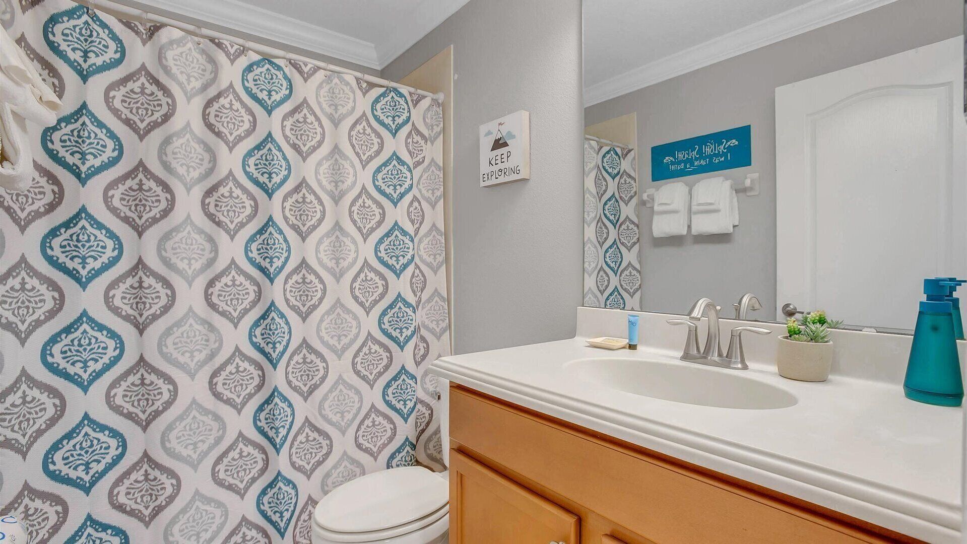 A bathroom with a patterned shower curtain, a sink with a mirror, and a sign that says "KEEP EXPLORING".