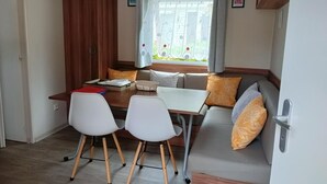 Ein gemütlicher Wohnbereich mit Esstisch, zwei Stühlen, einer Couch und einem Fenster mit Vorhängen.