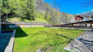 A grassy area with a stone pathway, a wooden fence, and a building with a red roof in the background.
