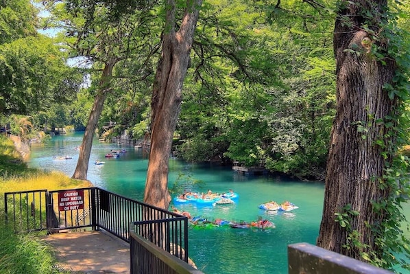 A river with people on rafts, surrounded by trees and a warning sign.