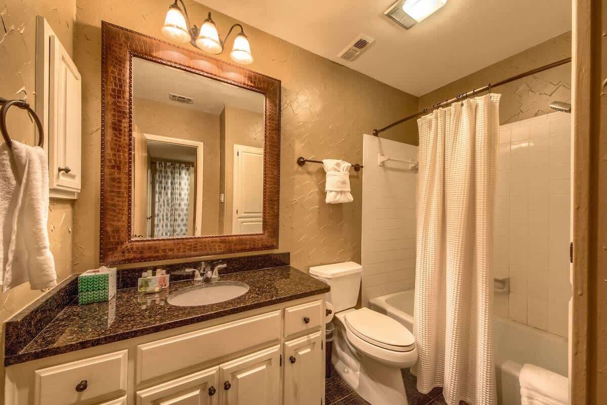 A bathroom with a sink, mirror, toilet, and shower curtain.