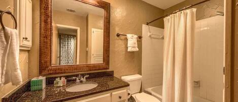 A bathroom with a sink, mirror, toilet, and shower curtain.