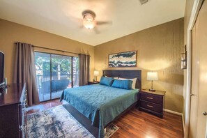 A bedroom with a bed, a nightstand, a lamp, a ceiling fan, and a view through a sliding door.