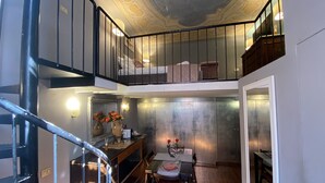 Ein mehrgeschossiges Interieur mit einer Treppe, einem Essbereich mit Tisch für zwei Personen und einem Wohnbereich mit Sofa und Fernseher.