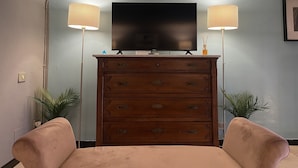 Ein Wohnzimmer mit Flachbildfernseher auf einer Holzkommode, zwei Lampen und einem Sofa.