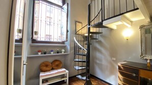 Eine Treppe mit schwarzer Geländer zum oberen Stockwerk, ein Fenster mit schmiedeeisernen Gitterstäben, eine weiße Bank mit Kissen und ein Holzboden.