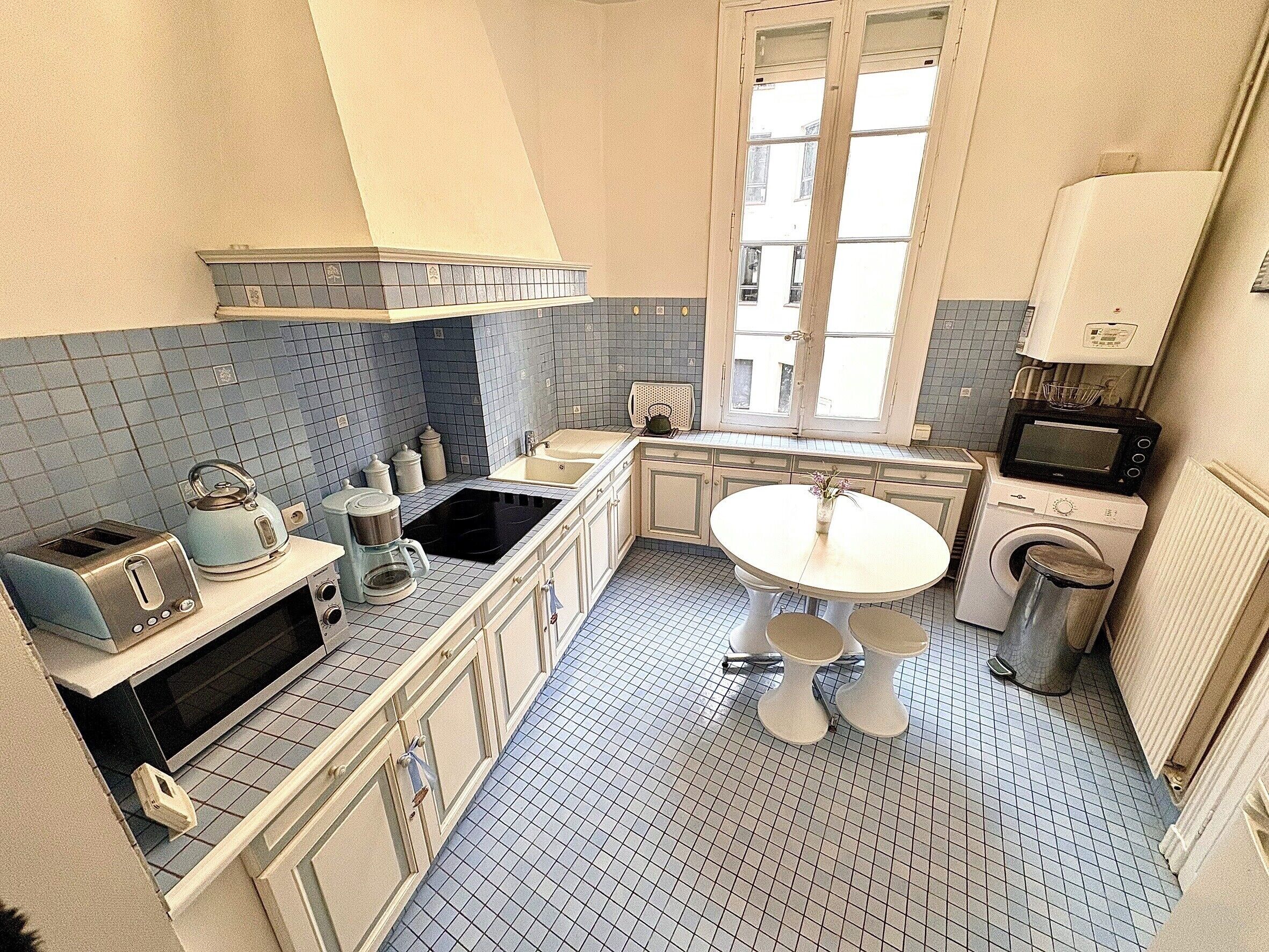 Een kleine keuken met een spoelbak, fornuis en een eettafeltje.