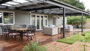 Eine überdachte Terrasse mit Holzboden, Gartenmöbeln und einem Gartenbereich.