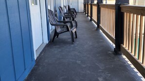 Een overdekte gang met rijen stoelen, een houten leuning en uitzicht op buiten.