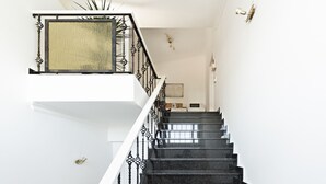 Un escalier avec des marches noires et une rampe noire ornée, menant à l’étage supérieur.
