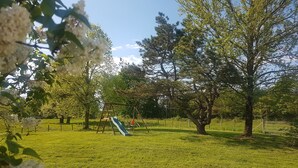 A grassy park area with trees, a playground, and a slide. - Maison Entre Prés et Bois (Marboz)