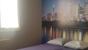 A bedroom with a cityscape mural, a bed with a headboard, a bedside table, and a window with blinds. - Maison Entre Prés et Bois (Marboz)