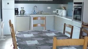 A compact kitchen with white cabinets, a microwave, a stove, and a sink. There is a dining table with chairs in the foreground. - Maison Entre Prés et Bois (Marboz)