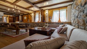 A cozy cabin interior with a wooden dining table, a sofa, and a stone wall.