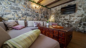 A cozy living room with a stone wall, a flat-screen TV mounted above a wooden dresser, and a comfortable sofa with cushions.