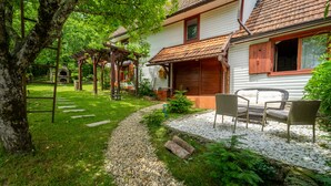 A rustic wooden house with a garden path leading to a seating area with wicker furniture.