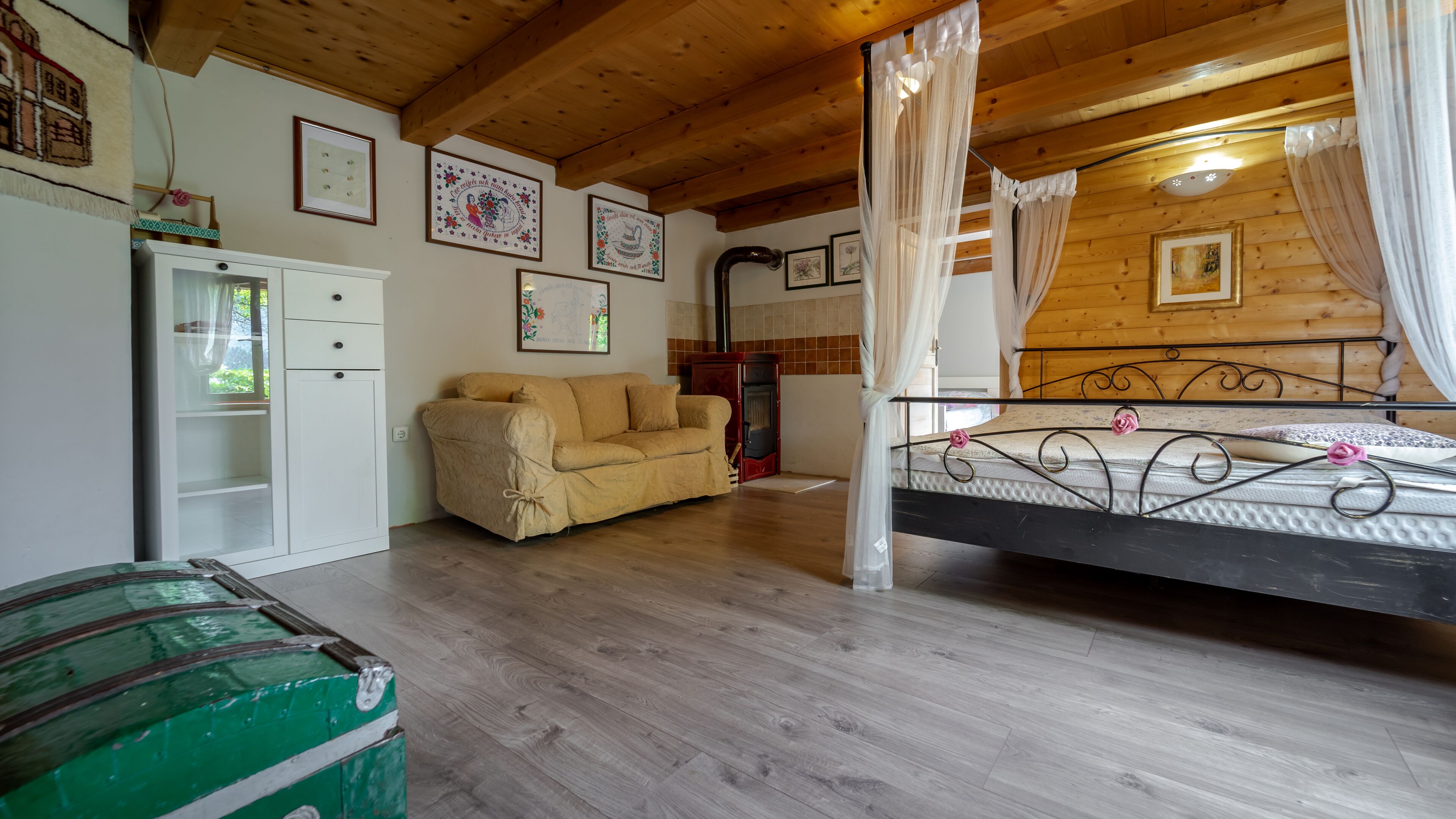 Une pièce chaleureuse avec un plafond en bois, un lit avec un cadre en métal, un canapé beige, une armoire blanche et une commode verte.