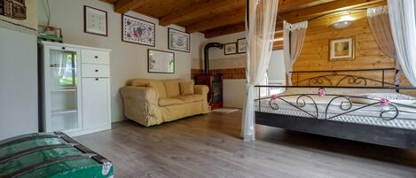Une pièce chaleureuse avec un plafond en bois, un lit avec un cadre en métal, un canapé beige, une armoire blanche et une commode verte.