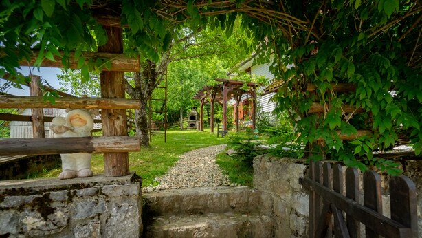 A rustic outdoor setting with a wooden pergola, a stone pathway, and a small brick oven.
