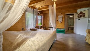 A wooden cabin bedroom with a bed, curtains, and a view of the outdoors.