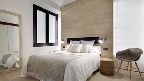 A modern bedroom with a large bed, a mirror, a wall-mounted light, and a wicker chair. - Luna by FeelFree Rentals (San Sebastian)