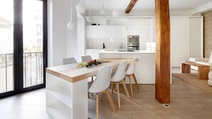 A modern kitchen with white cabinetry, a wooden dining table, and a large window. - Luna by FeelFree Rentals (San Sebastian)