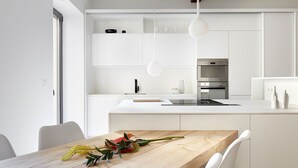 A modern kitchen with white cabinetry, a wooden dining table, and pendant lights. - Luna by FeelFree Rentals (San Sebastian)
