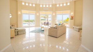 Een ruime woonkamer met een groot raam, een bank, een bijzettafeltje en uitzicht op het strand.