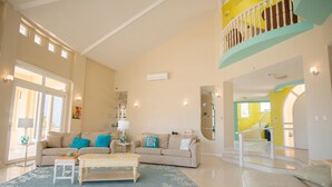 Een ruime woonkamer met een hoge plafond en een trap die leidt naar een hoger gelegen verdieping, plus een groot raam voor natuurlijk licht.