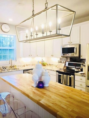 A kitchen with white cabinets, a wooden countertop, a hanging light fixture, and a microwave.