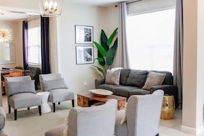 A modern living room with a grey sofa, two armchairs, a coffee table, and a dining area in the background.
