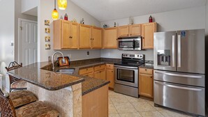 A modern kitchen with wooden cabinets, stainless steel appliances, a granite countertop, and pendant lighting. - Palm Breeze - Heated Private Pool, Deeded Beach Access, Free Beach Service! (Miramar Beach)