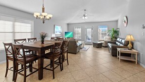 A spacious living room with a dining area, a ceiling fan, and a television. - Palm Breeze - Heated Private Pool, Deeded Beach Access, Free Beach Service! (Miramar Beach)